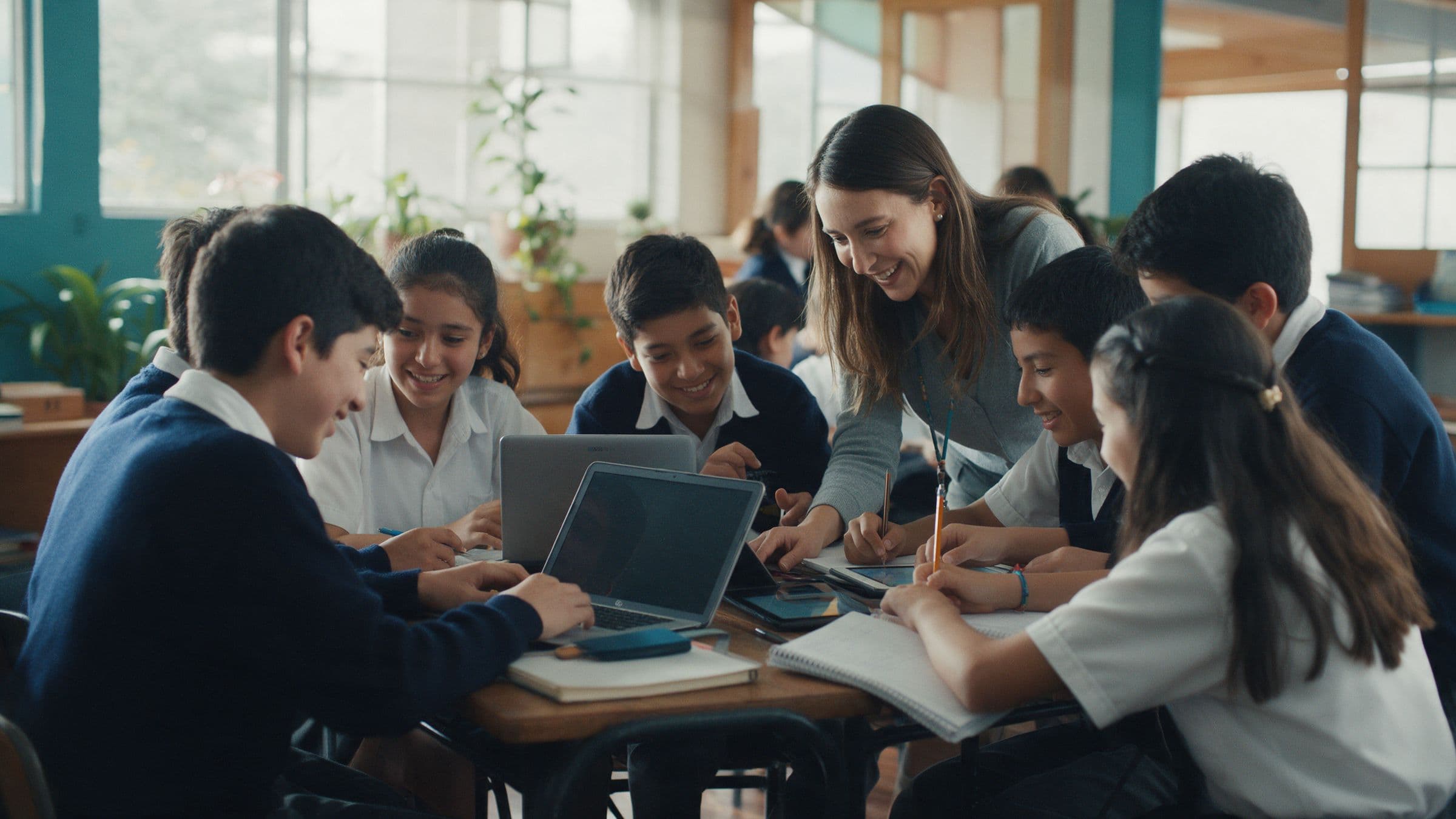 Estudiantes trabajan en equipo con laptops y cuadernos mientras su profesora los acompaña